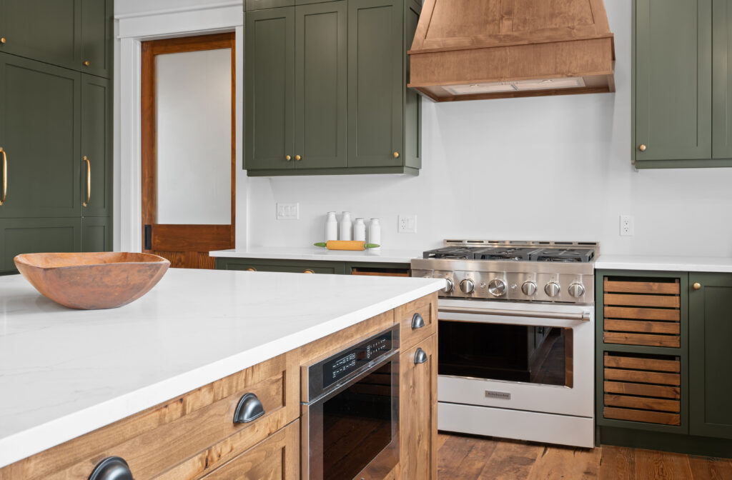 Custom kitchen with green shaker cabinets, wood range hood, and stone counters photographed for builders in Kingston Ontario