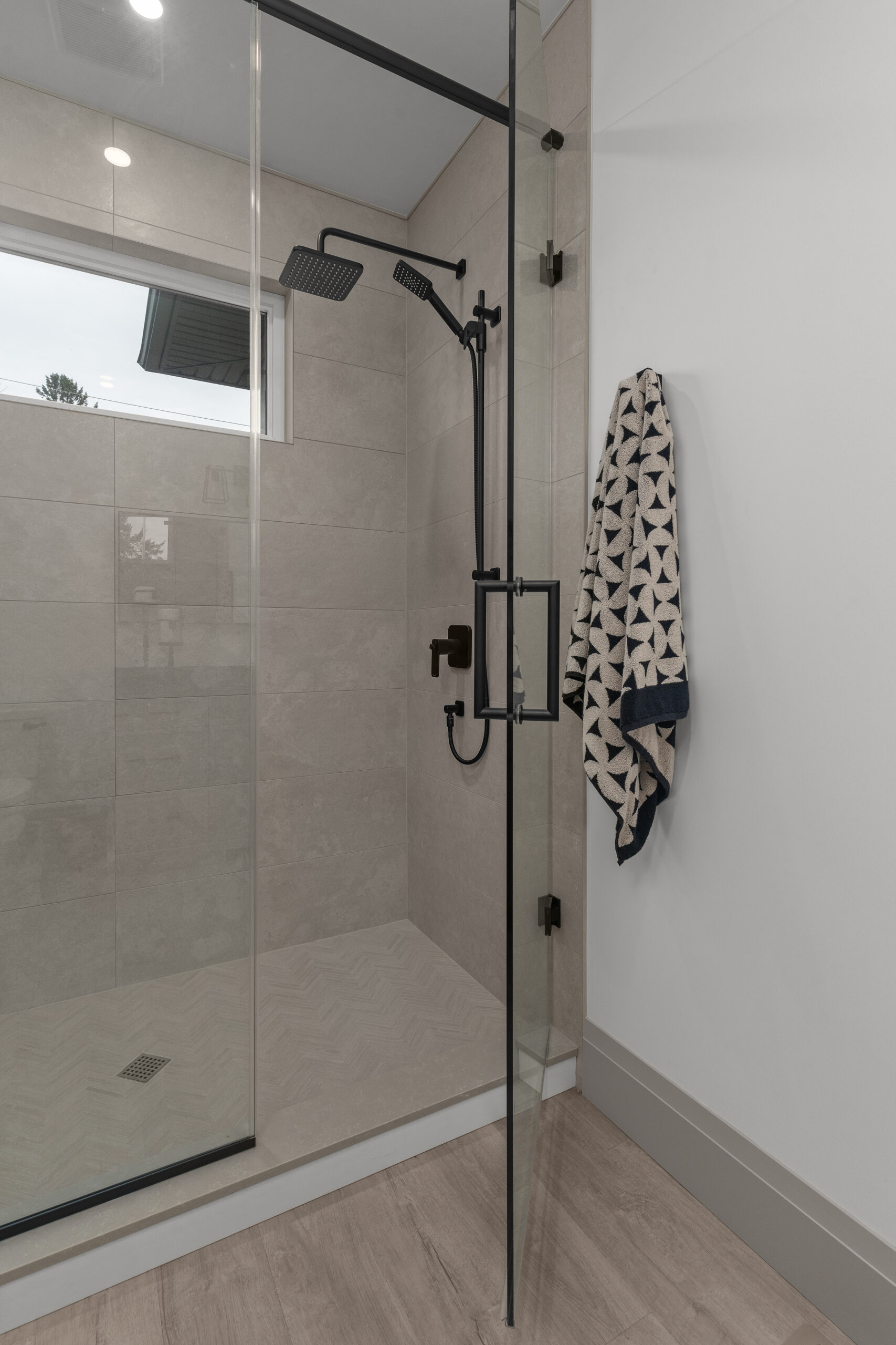 Modern bathroom with glass shower, neutral tile, and black fixtures photographed for a Kingston home builder