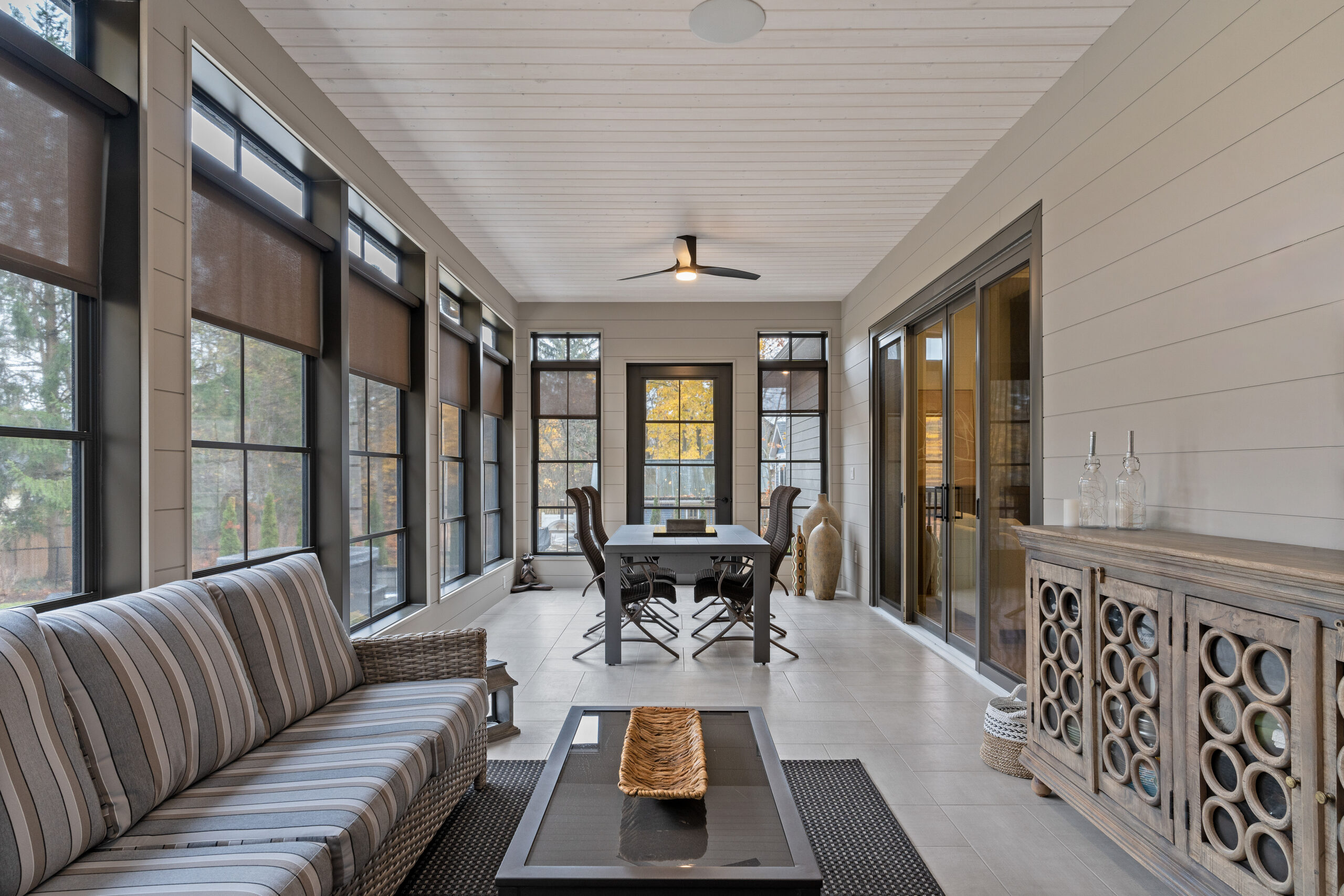 Bright four season sunroom with black framed windows, modern ceiling fan, and neutral decor photographed for a Kingston builder