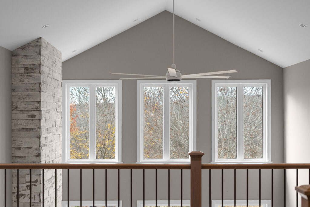 Vaulted ceiling with large windows, a modern ceiling fan, and a stone chimney