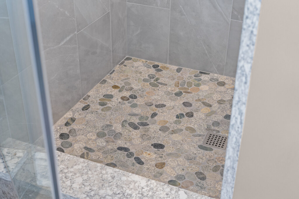 Close-up of a pebble mosaic shower floor with grey tile walls