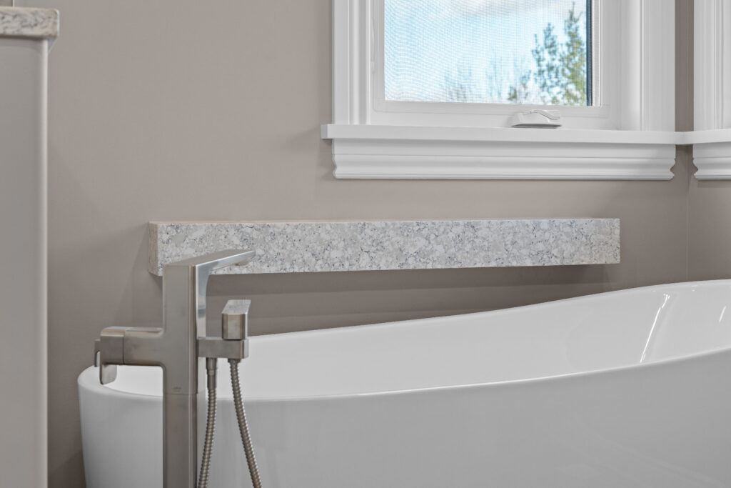 Modern freestanding bathtub with a floor-mount faucet and a quartz ledge by the window